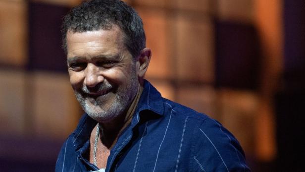 Antonio Banderas lächelt in einem dunkelblauen, gestreiften Hemd vor einem unscharfen Hintergrund.