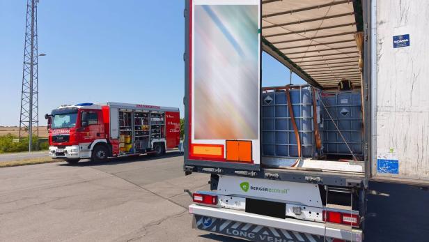 Feuerwehrwagen neben einem offenen Lkw mit IBC-Behältern an einer Landstraße.