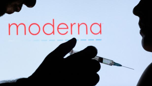 FILE PHOTO: People pose with syringe with needle in front of displayed Moderna logo