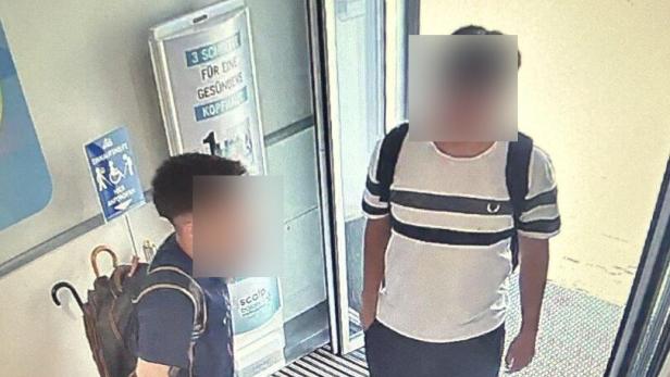 Zwei junge Männer mit Rucksäcken stehen im Eingangsbereich vor einer Glastür.