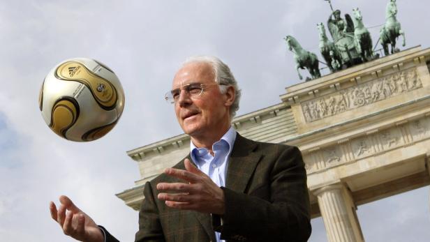 Franz Beckenbauer vor dem Brandenburger Tor mit einem Fußball.