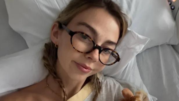 Sydney Towle mit einer Brille auf der Nase liegt in einem Bett