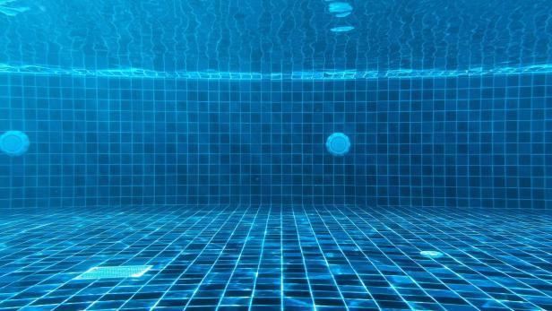 Leere Unterwasseransicht eines Freibadbeckens mit blau gekacheltem Boden und Wasseroberfläche.