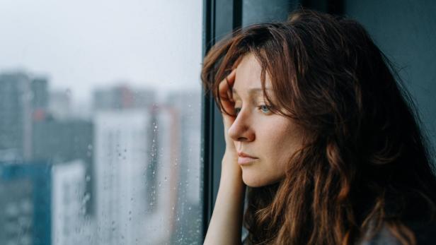 Nachdenkliche Frau mit langem Haar schaut regnerisch aus dem Fenster.