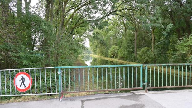 Bewaldeter Kanal hinter einer gesperrten Brücke mit Fußgängerverbotsschild.