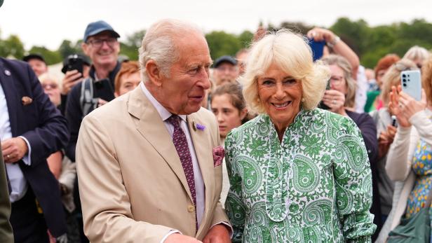 König Charles III. und Königin Camilla lächeln bei einem öffentlichen Auftritt in eine Menschenmenge.
