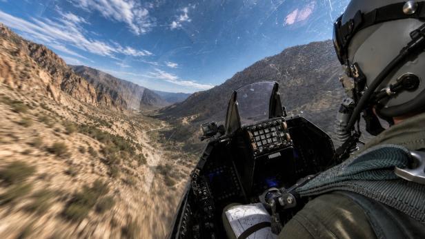 Blick aus dem Cockpit eines Kampfjets über ein schmales Gebirgstal.