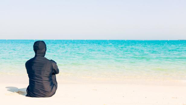 young woman wearing burkini sitting by the beach