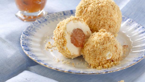 Marillenknödel mit Bröseln auf einem Teller, daneben ein kleines Glas mit Aprikosenkonfitüre auf einem blauen Tuch.