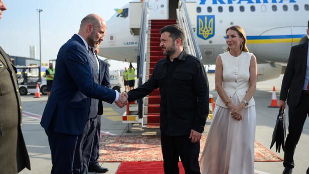 Selenskyj begrüßt einen Mann per Handschlag vor einem ukrainischen Regierungsflugzeug auf dem Rollfeld.