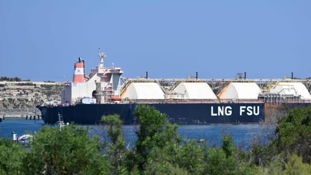 Ein LNG-Schiff mit großen Tanks liegt vor einer Küste im Hafen.