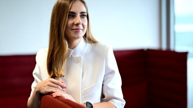 Simone Stribl in weißer Jacke sitzt an einem roten Stuhl und blickt nach rechts.