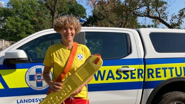 Eine lächelnde Rettungskraft steht vor einem Wasserrettungs-Pickup und hält ein gelbes Rettungsbrett.