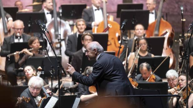 Ein Dirigent leitet ein Orchester mit Streichern und Bläsern auf der Bühne.