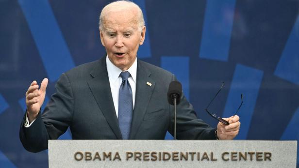 US-Präsident Joe Biden spricht am Rednerpult des Obama Presidential Center und hält eine Brille in der Hand.