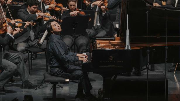 Lang Lang spielt konzentriert auf einem Steinway & Sons Flügel vor einem begleitenden Orchester.