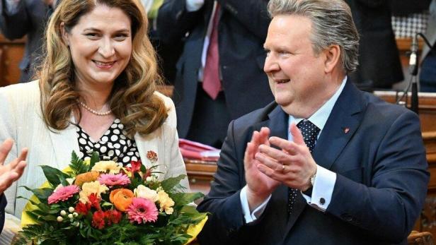 Eine Frau hält einen Blumenstrauß, daneben klatscht ein Mann im Anzug in einem feierlichen Saal.