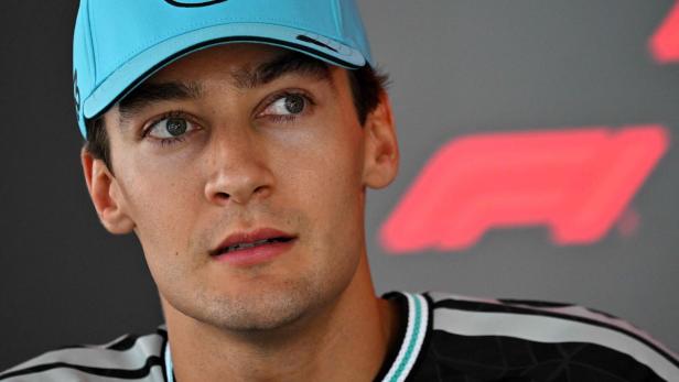 George Russell trägt eine hellblaue Mercedes-Kappe vor einem F1-Hintergrund.
