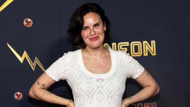 Tallulah Willis lächelt vor einem dunklen Hintergrund mit goldenen Blitz-Symbolen in die Kamera.