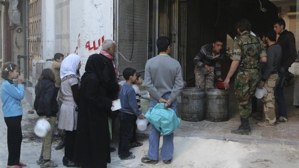 Eine Gruppe von Menschen steht Schlange, um Essen aus großen Fässern zu erhalten.