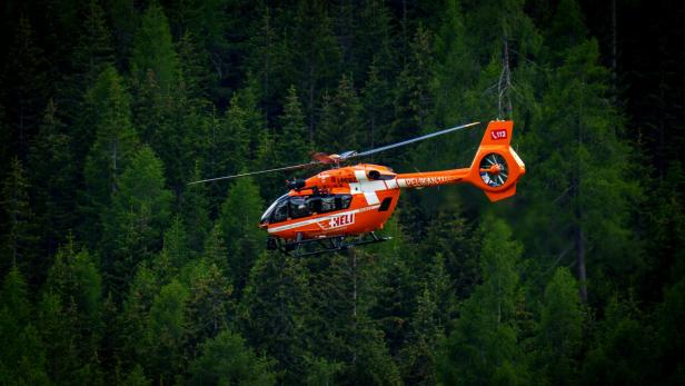 Ein orangefarbener Hubschrauber fliegt über einen dichten grünen Wald