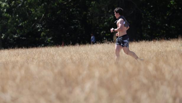 Ein barfüßiger Mann joggt durch ein trockenes Grasfeld vor dunklem Wald.