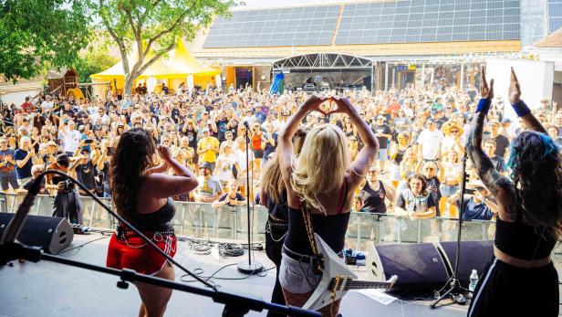 Band auf einer Open-Air-Bühne vor jubelnder Menschenmenge, die Sängerinnen begrüßen das Publikum.