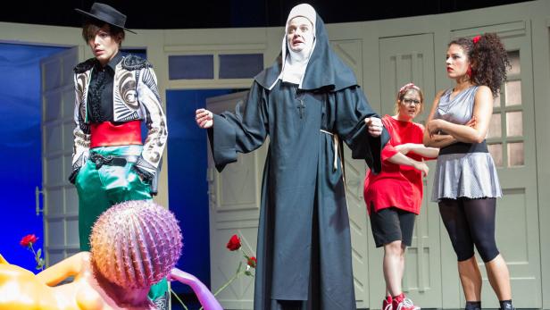 Eine Theaterszene mit einer Nonne, einem Torero und weiteren Darstellern auf einer Bühne.