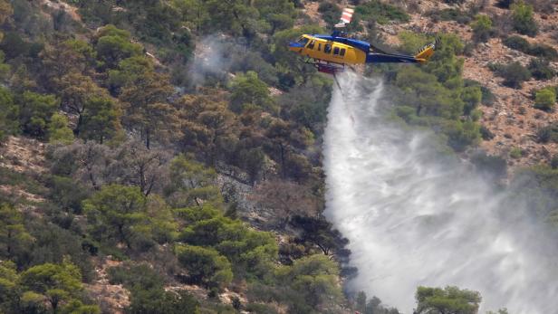 Ein Hubschrauber löscht einen Waldbrand und lässt Wasser auf den bewaldeten Hang nieder.