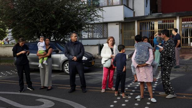 Mehrere Erwachsene und Kinder stehen auf einer Straße vor einem Wohnhaus und warten.
