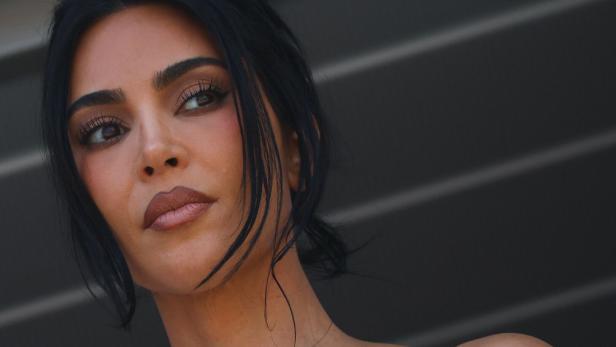 Kim Kardashian blickt mit dunklem Haar und dezentem Make-up nachdenklich zur Seite.