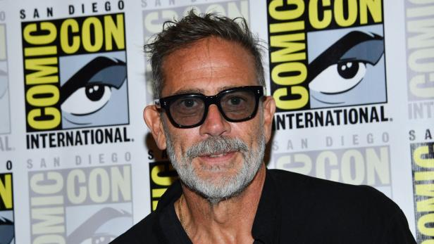Jeffrey Dean Morgan mit Brille und grauem Bart vor einer Comic-Con-Hintergrundwand.