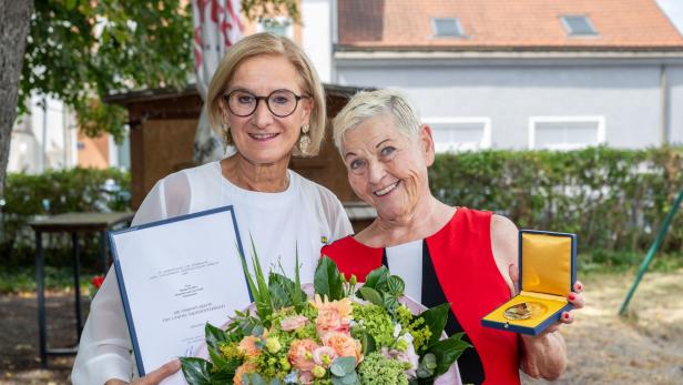 Johanna Mikl-Leitner überreicht Jazz Gitti Urkunde, Medaille und Blumen.