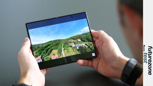 Person hält ein aufgeklapptes Falt-Handy mit Landschaftsvideo auf dem Display.