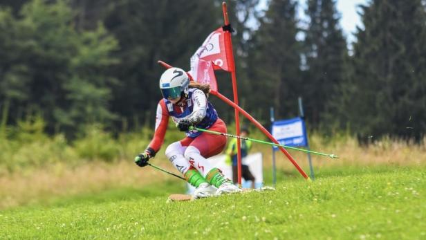 Skirennfahrerin in Rennhaltung durchfährt einen Slalom zwischen Toren auf einer Wiese.
