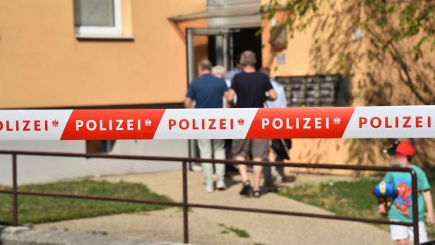Polizeisperre vor einem Wohnhaus, dahinter gehen Menschen zum Eingang.