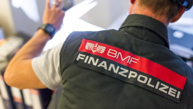 Ein Finanzpolizist mit erhobener Hand in Uniform mit der Aufschrift BMF und FINANZPOLIZEI.