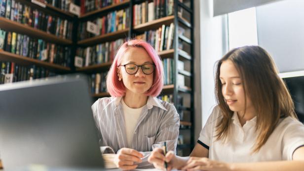 Female Tutor Helping Teen Student With Homework in Library
