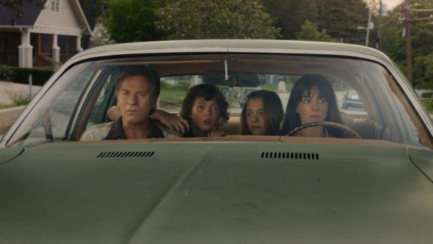 Ewan McGregor und Anne Hathaway sitzen mit zwei Kindern in einem grünen Auto und blicken ernst nach vorne.
