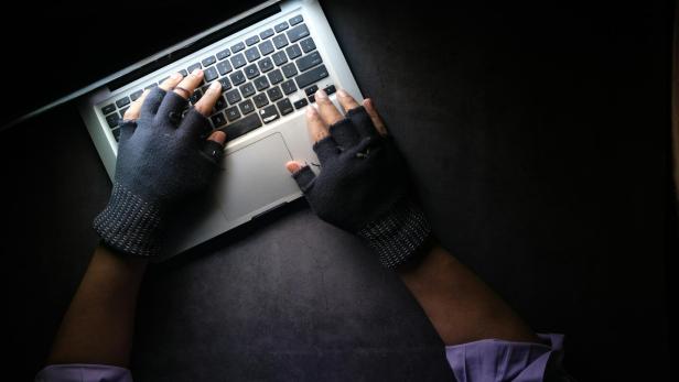 Hände in Fingerloshandschuhen tippen auf einem Laptop.