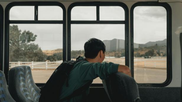 Junge mit Rucksack sitzt allein im leeren Bus und blickt aus dem Fenster.