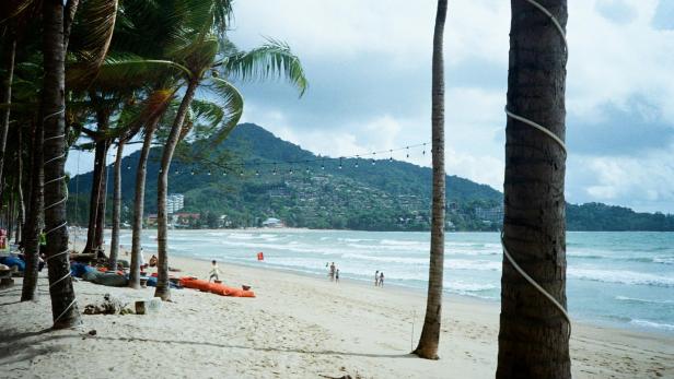 Strand mit Palmen, roter Warnflagge und hohen Wellen.