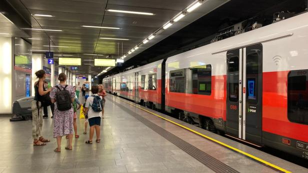 Fahrgäste stehen an einem Bahnsteig neben einem stehenden ÖBB-Zug.