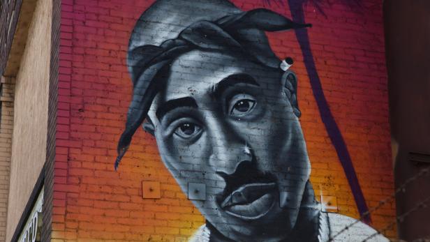 Graffiti-Porträt von Tupac Shakur auf einer Ziegelwand mit farbigem Hintergrund.