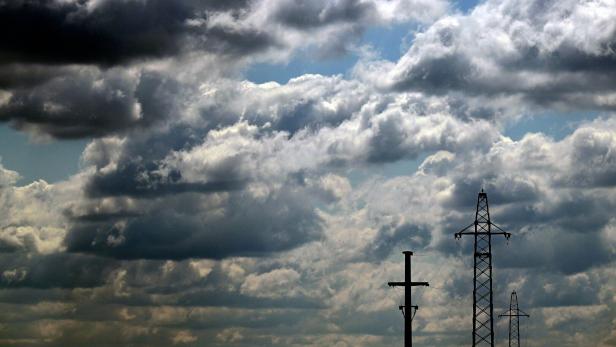Strommasten ragen vor einem dramatischen, wolkenverhangenen Himmel in die Höhe.