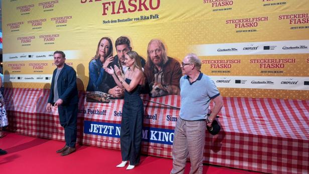 Sebastian Bezzel, Simon Schwarz und Lisa Maria Potthoff posieren bei der Premiere von „Steckerlfischfiasko“ vor dem roten Teppich in Wien.