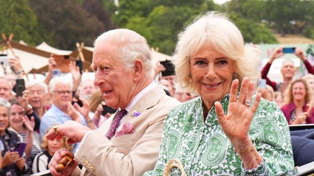 König Charles III. und Königin Camilla winken in einer Kutsche einer Menschenmenge zu.