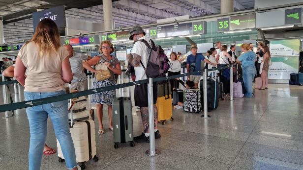 Reisende stehen mit Koffern in einer Warteschlange am Check-in des Flughafens.
