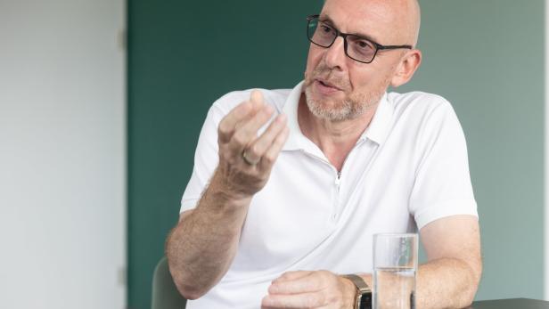 Ein Mann mit Brille spricht am Tisch und gestikuliert, neben ihm steht ein Wasserglas.