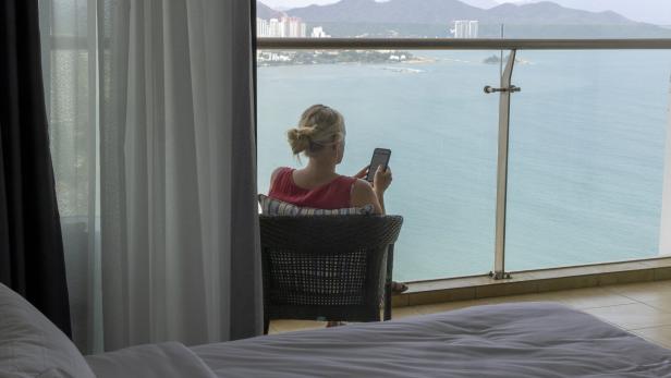 Mature woman uses mobile phone on balcony above city